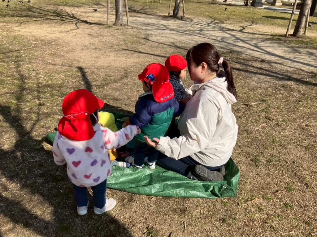 土佐稲荷公園でレジャーシートを広げて日向ぼっこをする園児と保育士