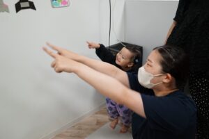 壁面の絵を指さしながら歌を歌う園児と保育士