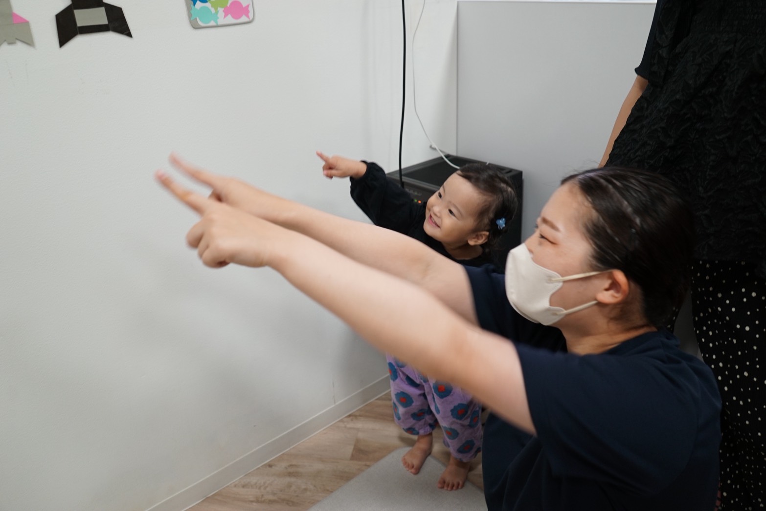 壁面の絵を指さしながら歌を歌う園児と保育士