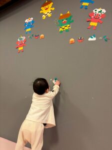 壁面の節分の絵を貼るお手伝いをする1歳児
