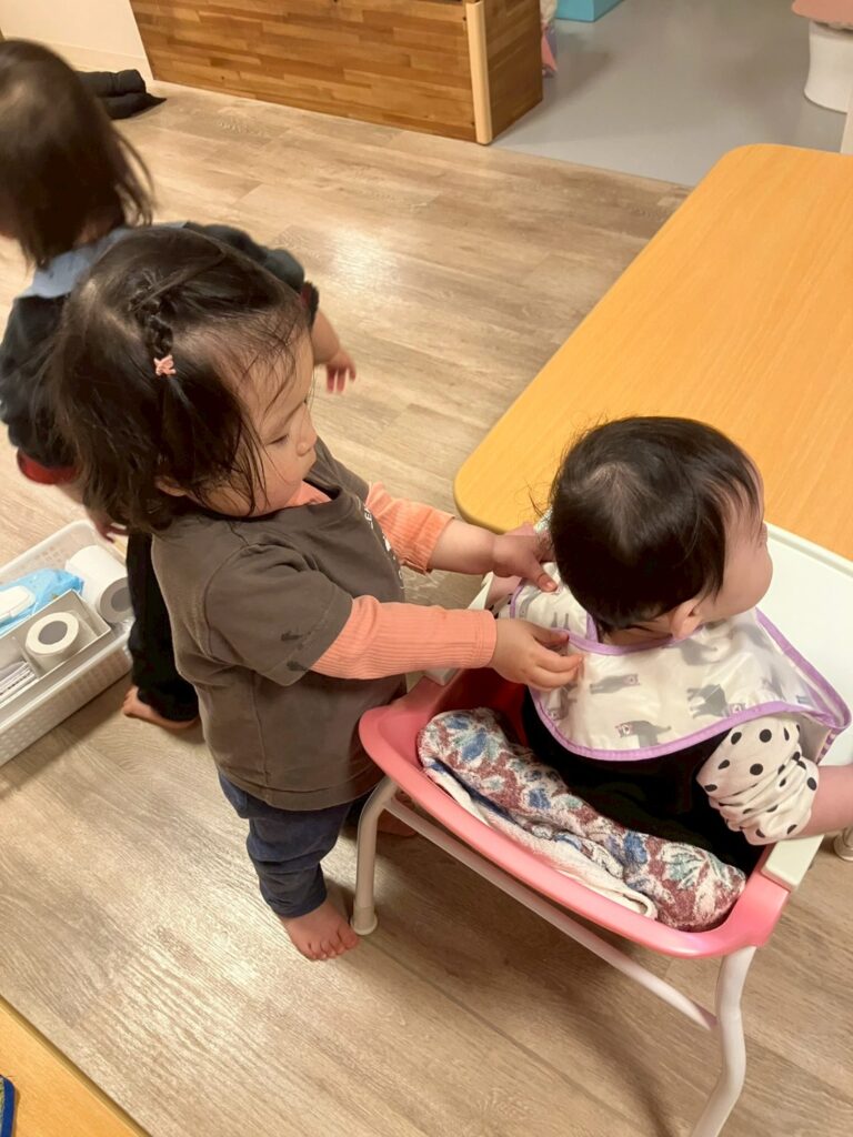 お友達のエプロンをつけてあげる園児