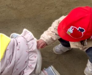 お友達のお尻についた砂を掃ってあげる園児