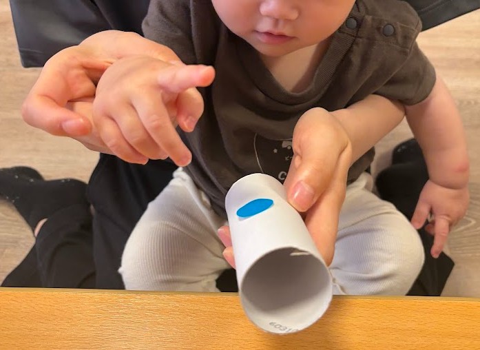 トイレットペーパーの芯にシールを保育士と貼る園児