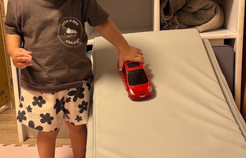 保育士の手作りの坂道で車を走らせる園児