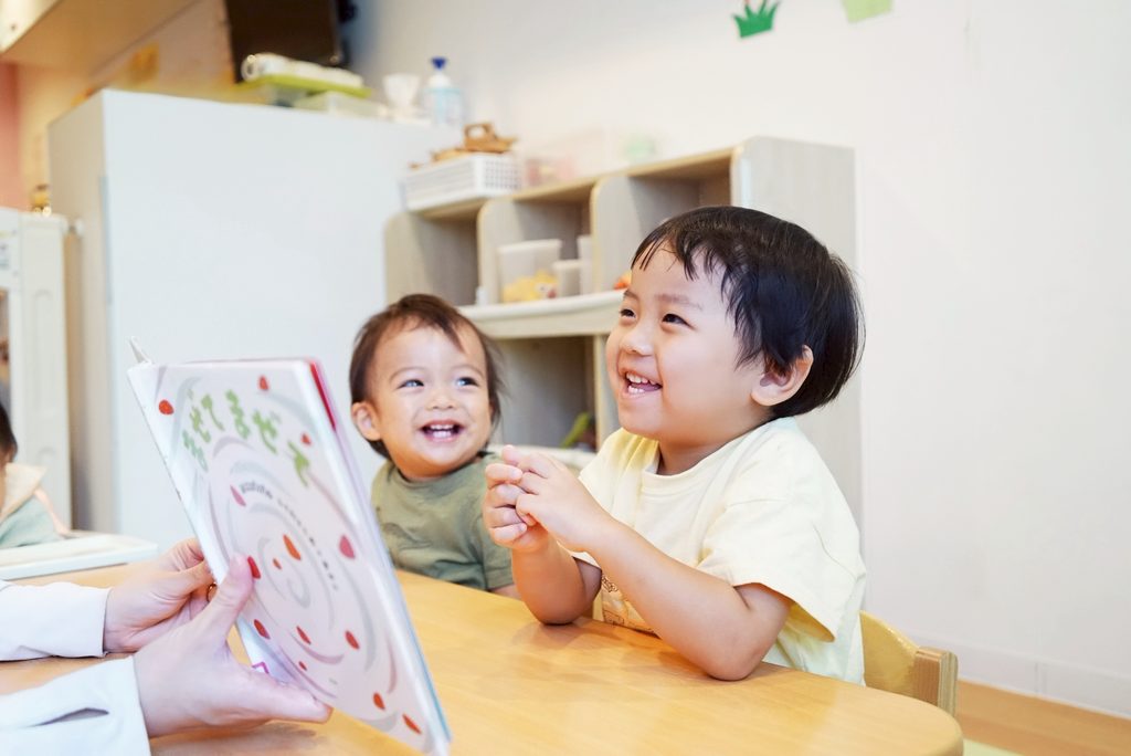 PEEK A BOO保育園で絵本を読んでもらって楽しそうな0歳児と2歳児